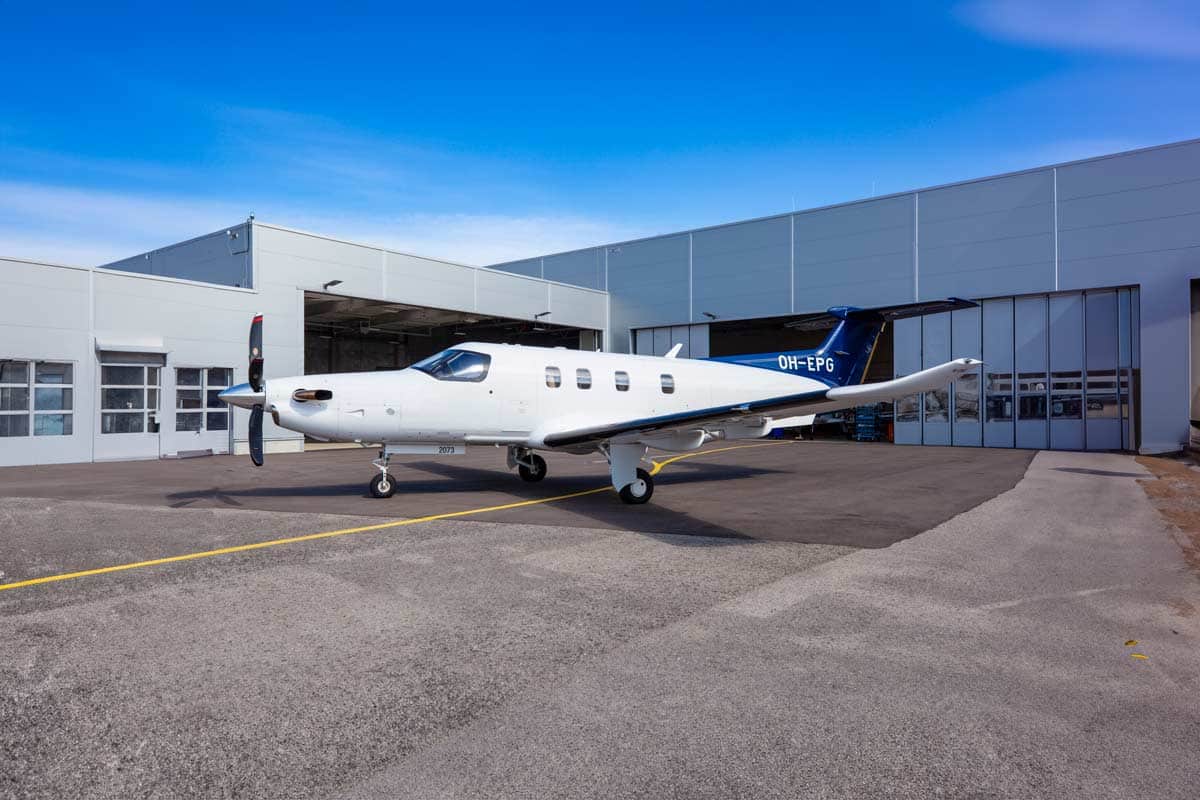 A small white and blue private aircraft parked outside a hangar on a sunny day.