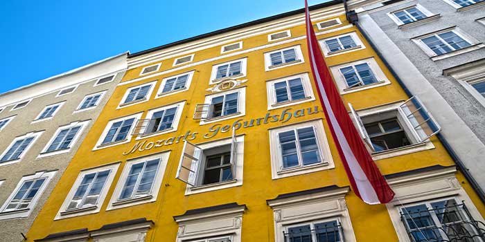 Yellow building with "Mozarts Geburtshaus" written on it; features multiple windows and a red and white flag hanging down.