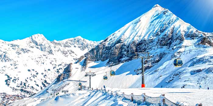 Snow-covered mountains with ski lifts ascending. Bright blue sky above.