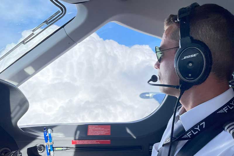 Der Pilot trägt ein Headset und blickt während des Fluges aus dem Cockpitfenster auf die Wolken.