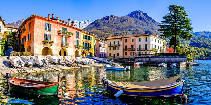 Colorful boats docked along a picturesque waterfront with vibrant buildings and a mountain backdrop under a clear blue sky.