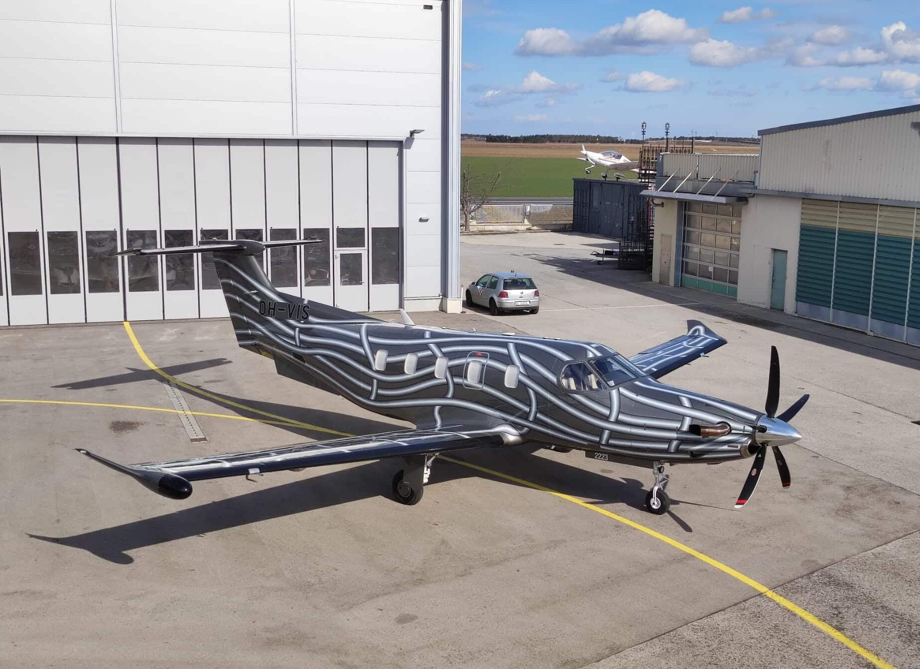 Kleines Flugzeug mit Streifenmuster, das an einem sonnigen Tag vor einem Hangar geparkt ist.